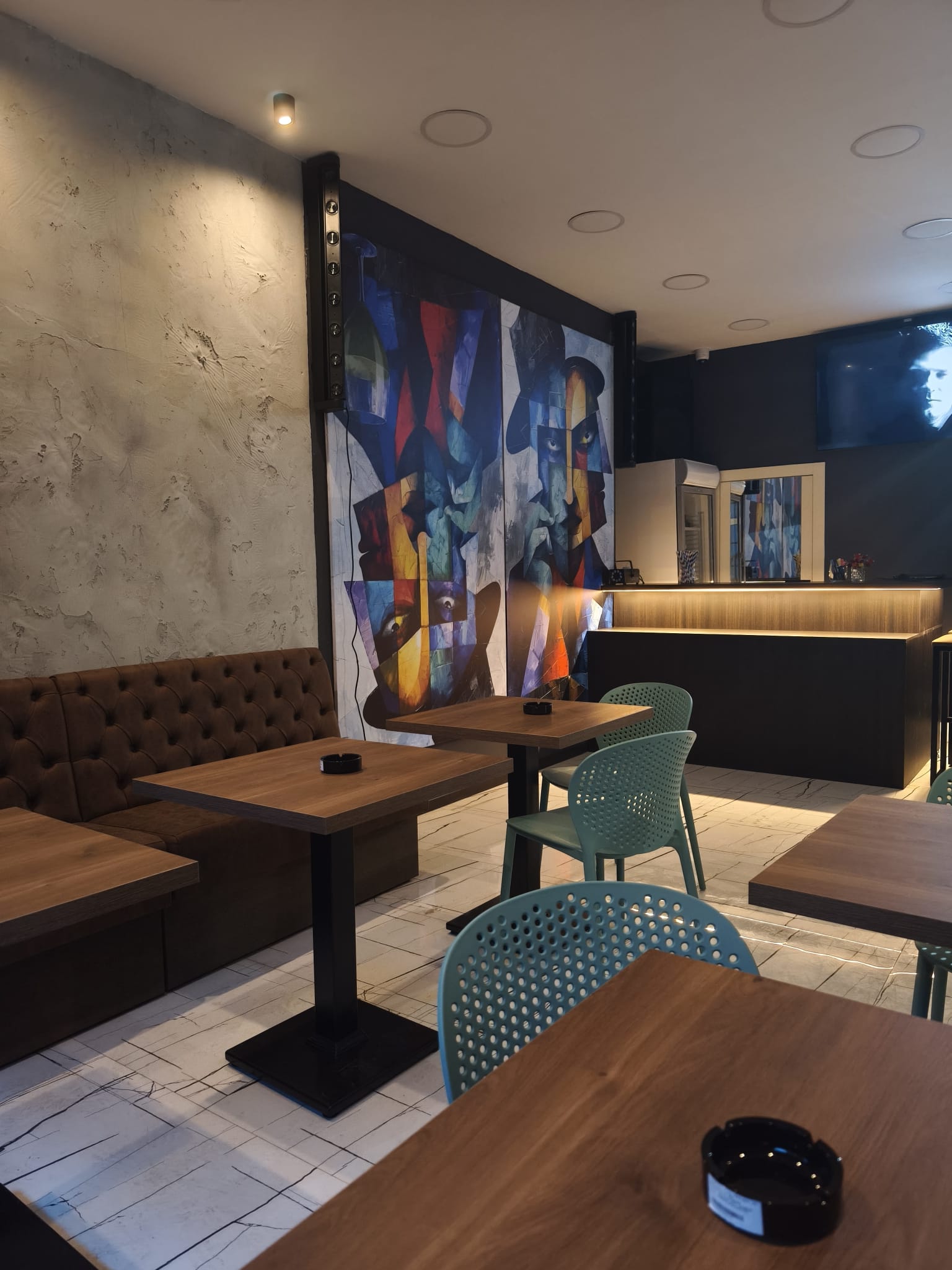 Kubistički mural, stolovi i osvetljeni šank u Paradox Kafeu